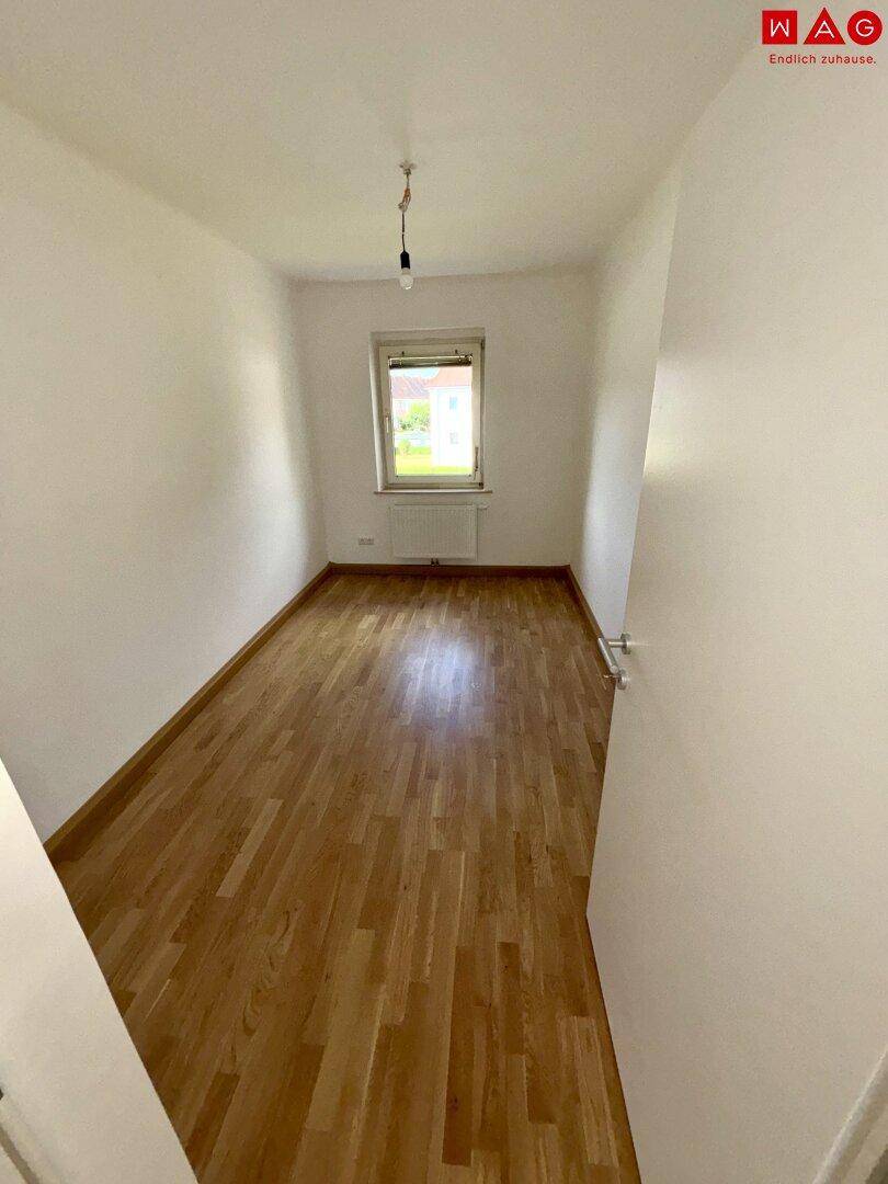 Gemütliches, leeres Schlafzimmer mit hellem Parkettboden und einem Fenster.