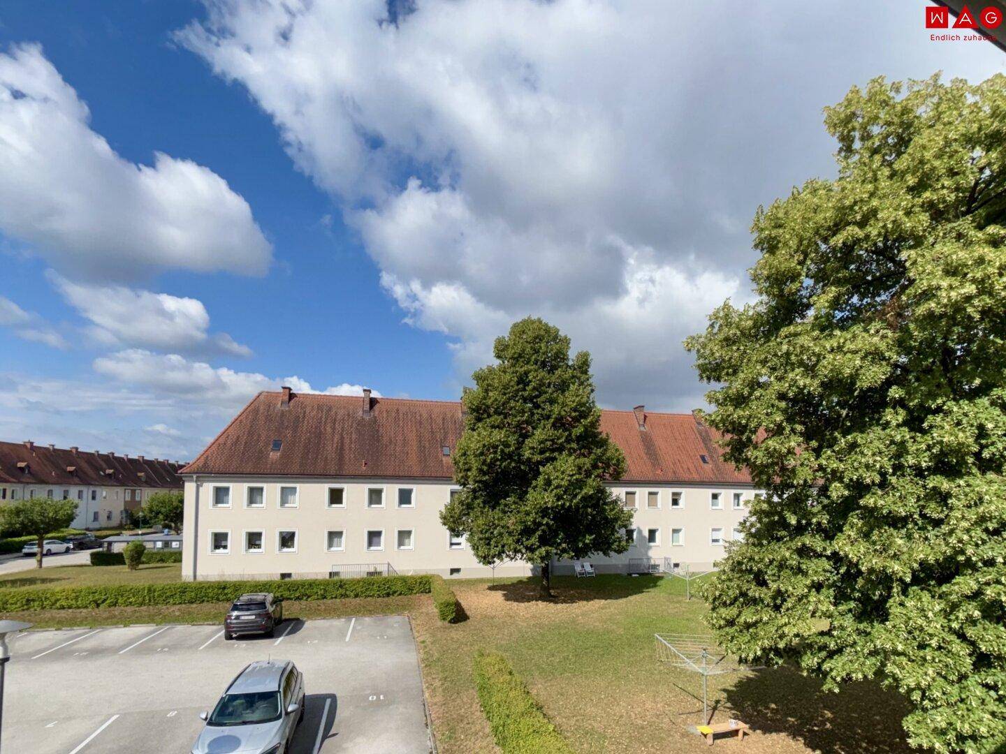 Ansicht eines großen Wohngebäudes mit rotem Dach, umgeben von Bäumen und Parkplätzen.