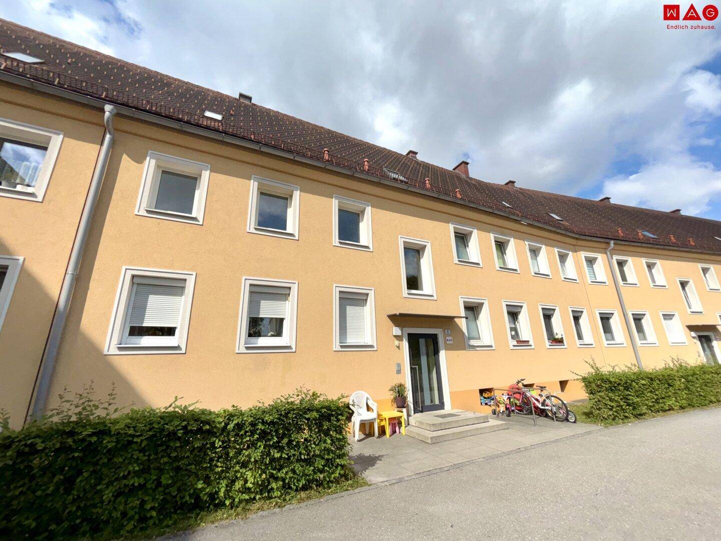 Seitenansicht der gelben Gebäudefassade mit Eingangstür und Fahrrädern davor.