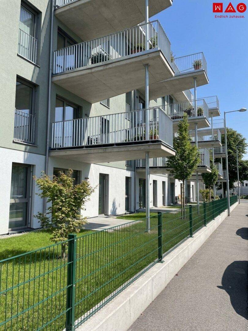 Moderne Wohnanlage mit mehreren Balkonen und privaten Gärten im Erdgeschoss, umgeben von Grün.