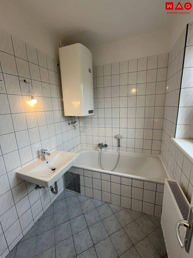 Helles Badezimmer mit weißen Fliesen, Badewanne, Waschbecken und einem Fenster für Tageslicht.