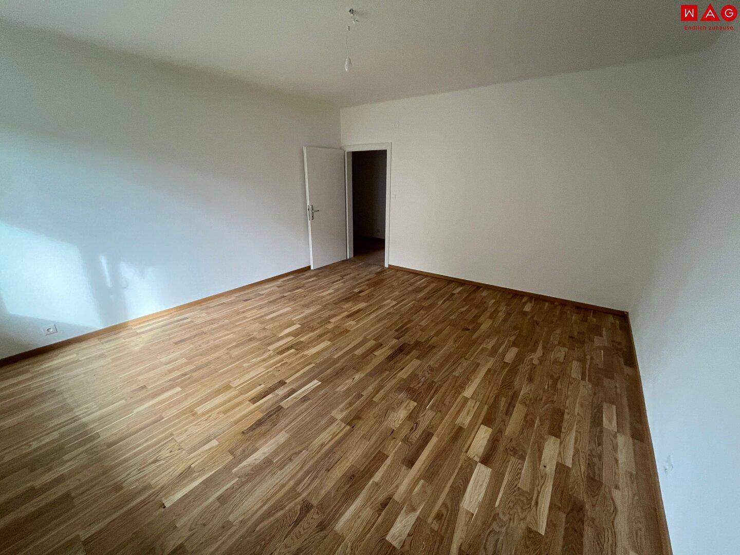 Geräumiger, leerer Raum mit Holzboden und weiß gestrichenen Wänden, bereit zur Einrichtung.
