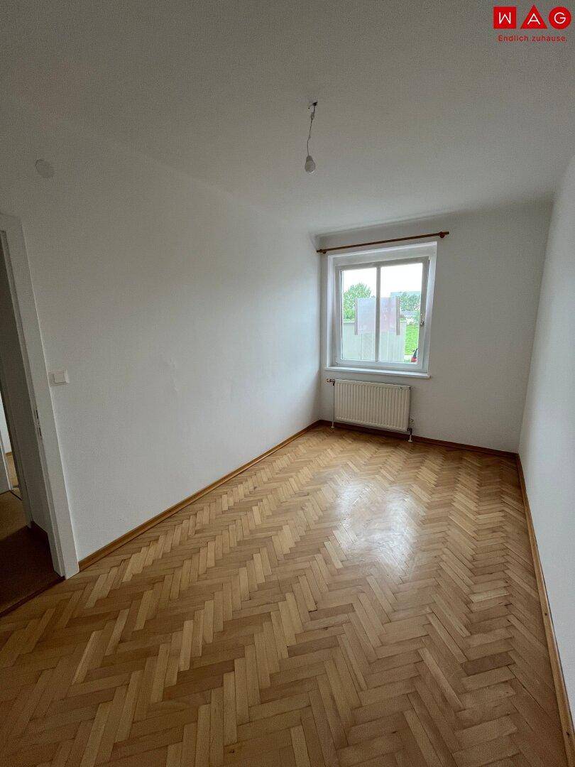 Leeres Schlafzimmer mit Fischgrätparkett und einem Fenster, das viel Licht hereinlässt.