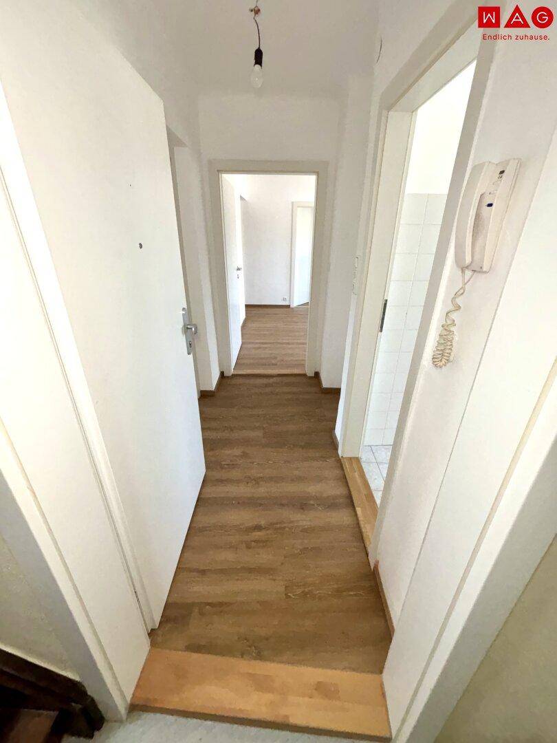 Langer, schmaler Flur mit Laminatboden und weißen Türen, der zu weiteren Räumen führt.
