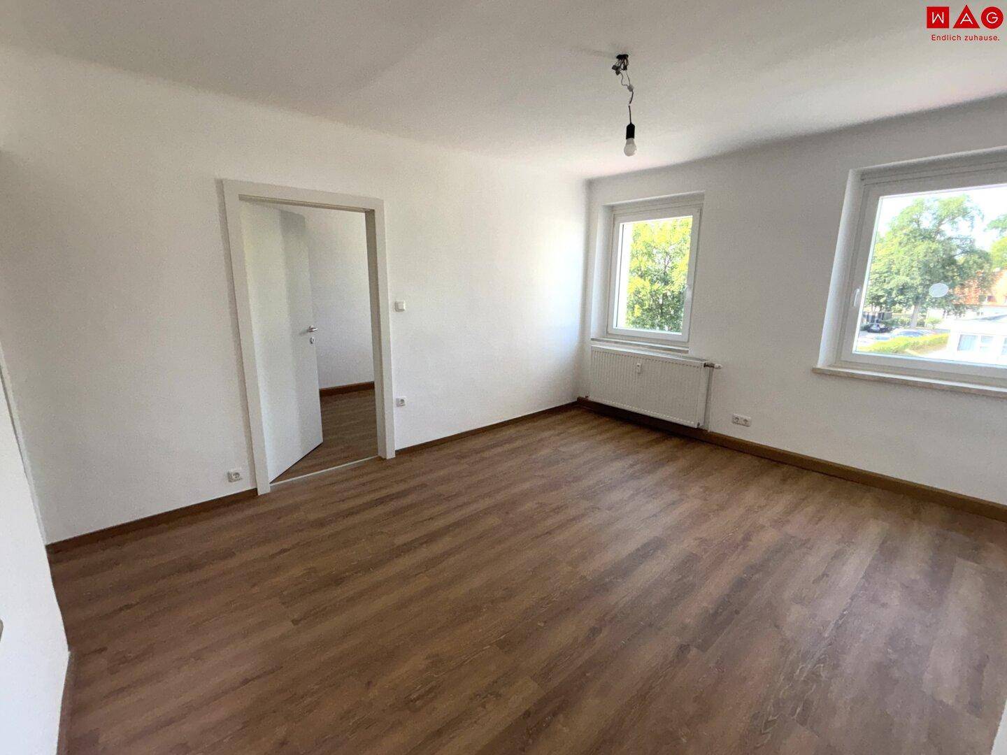 Geräumiges Zimmer mit Laminatboden und zwei Fenstern, die viel Tageslicht hereinlassen.