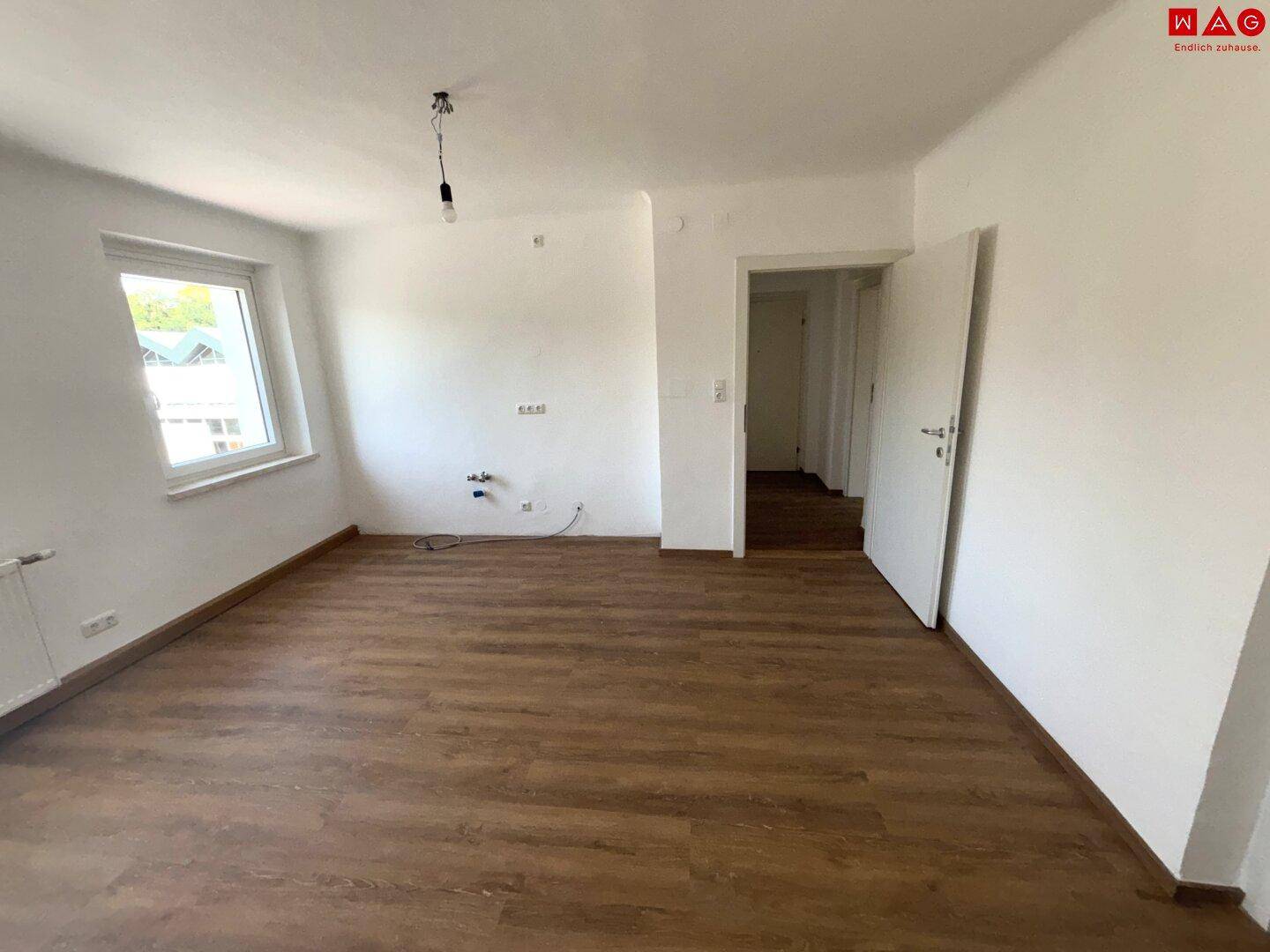 Leerer Raum mit Laminatboden und Anschlüssen für eine Küche, bereit für die Installation.