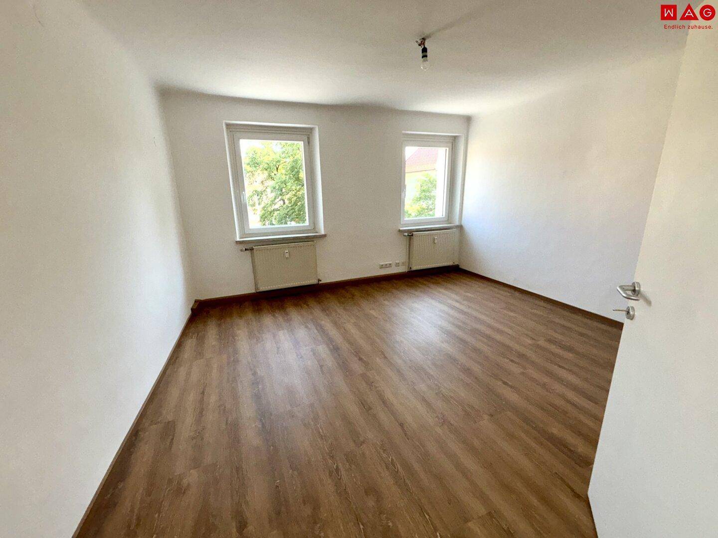 Geräumiges Schlafzimmer mit Laminatboden und zwei Fenstern, die einen Blick ins Grüne bieten.