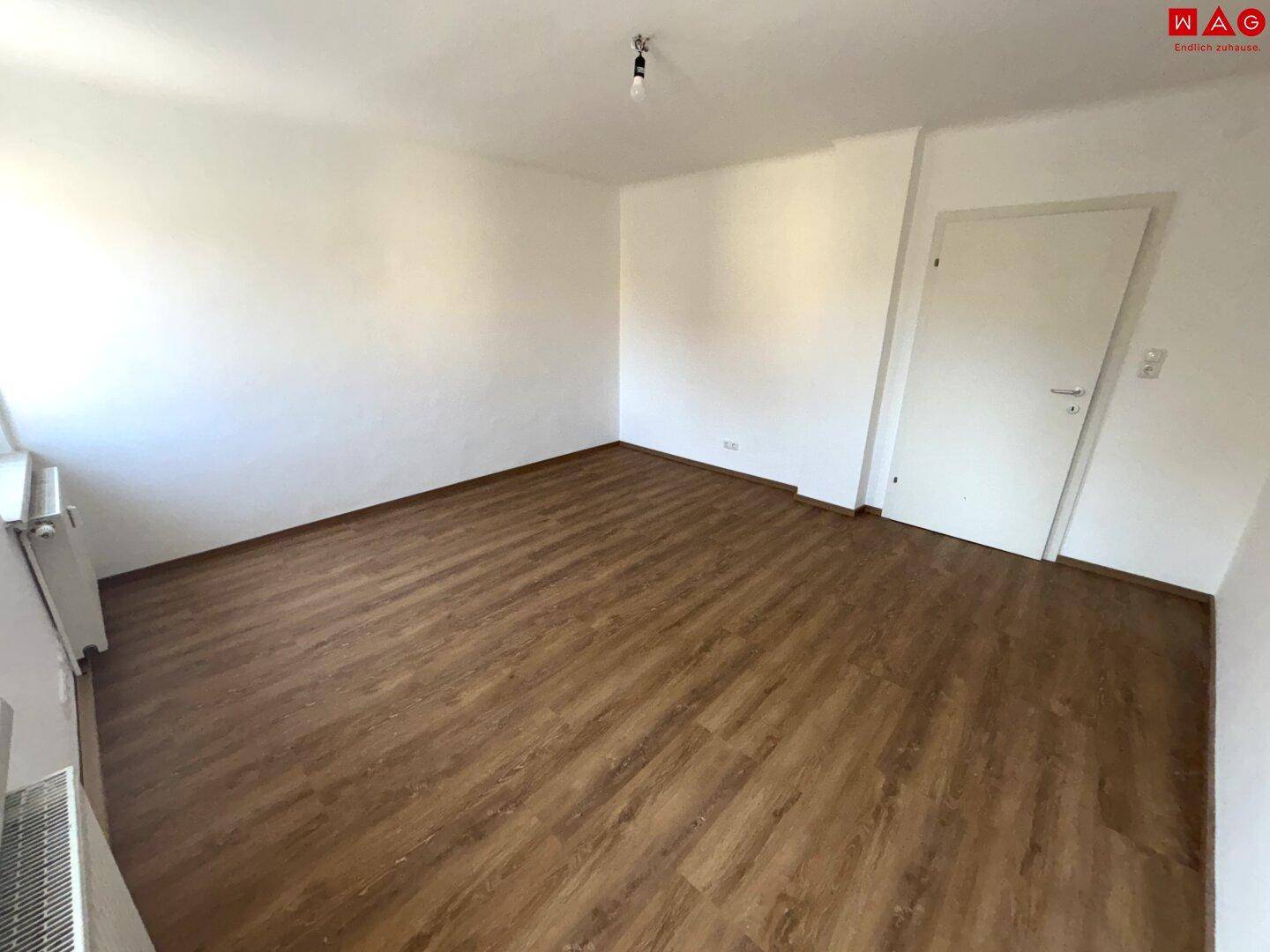 Helles Zimmer mit Laminatboden und weiß gestrichenen Wänden, ideal als Schlaf- oder Arbeitszimmer.