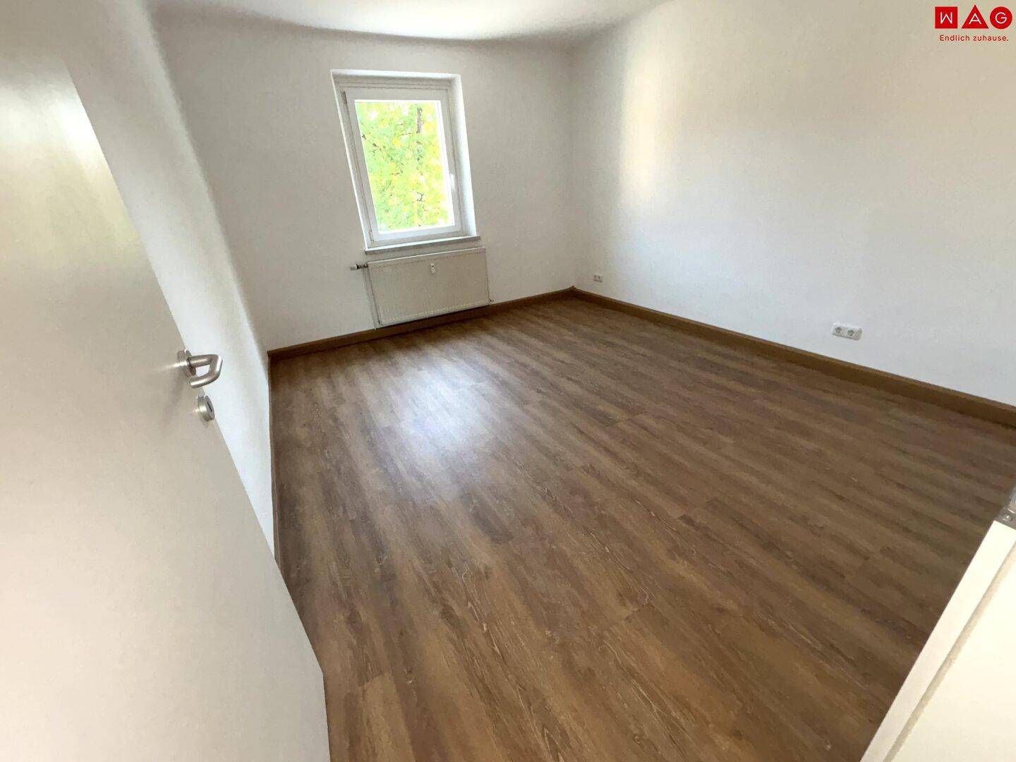 Helles Zimmer mit Laminatboden und einem Fenster, das einen angenehmen Ausblick bietet.
