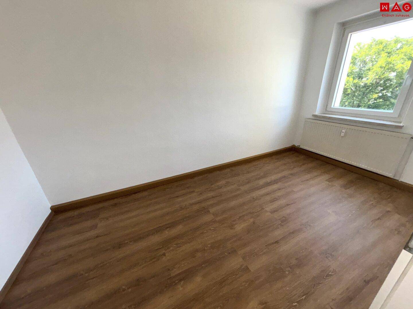 Helles Zimmer mit Laminatboden und einem Fenster, das viel Tageslicht in den Raum bringt.