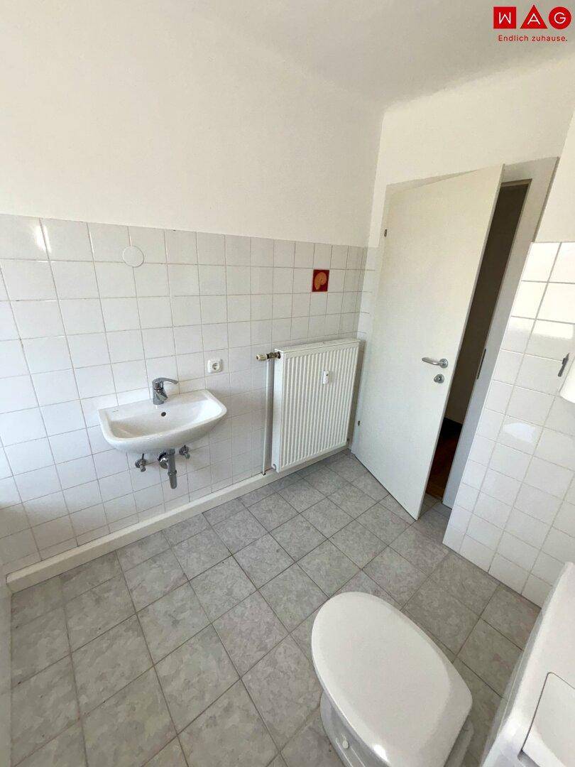 Badezimmer mit Waschbecken, WC und Heizkörper, gefliest in Weiß mit roten Akzenten.