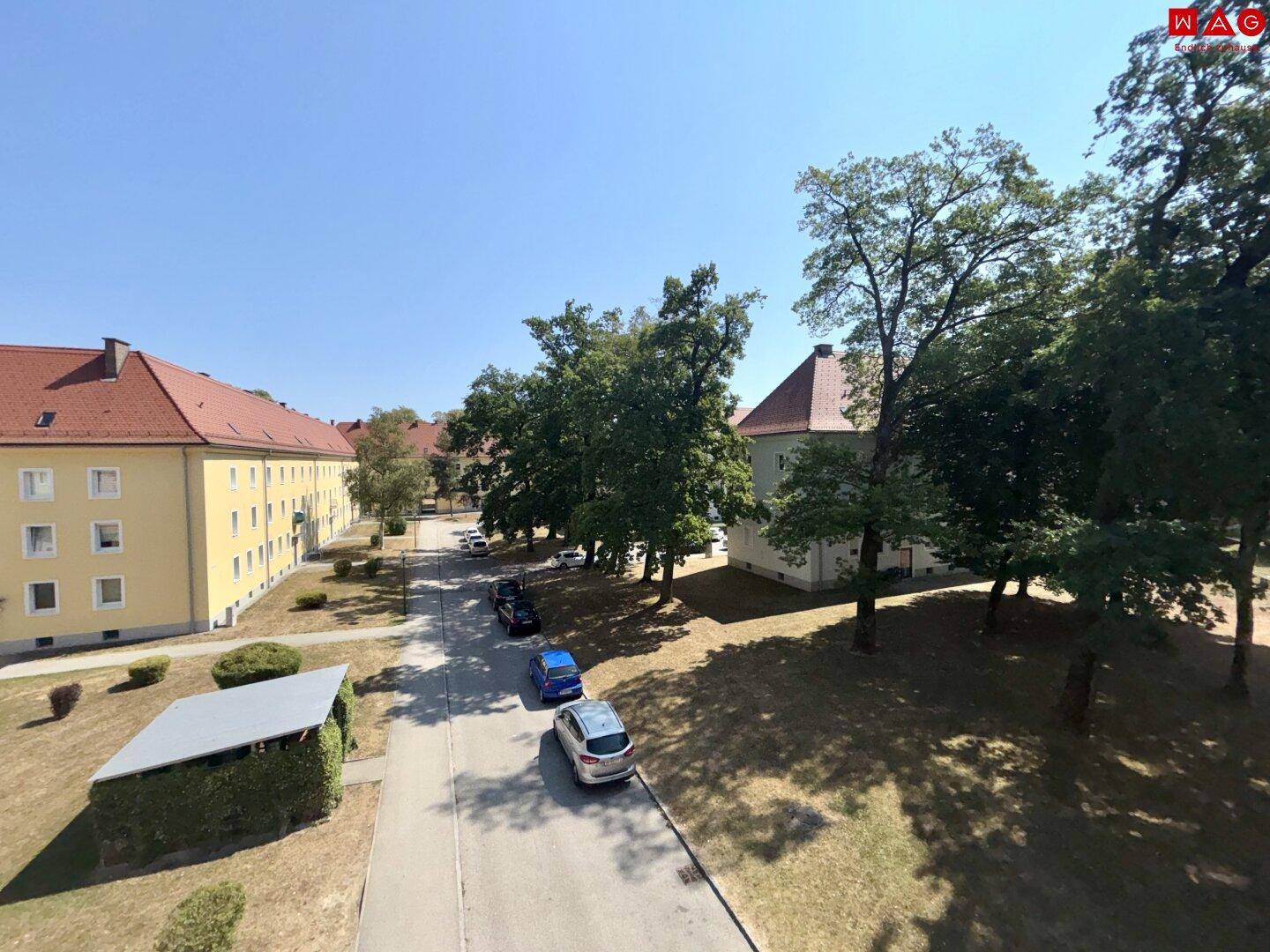 Blick von oben auf die Wohnanlage mit Bäumen, Parkplätzen und umliegenden Gebäuden.