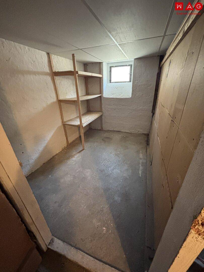 Kellerraum mit Betonboden, kleinem Fenster und Holzregalen für zusätzlichen Stauraum.
