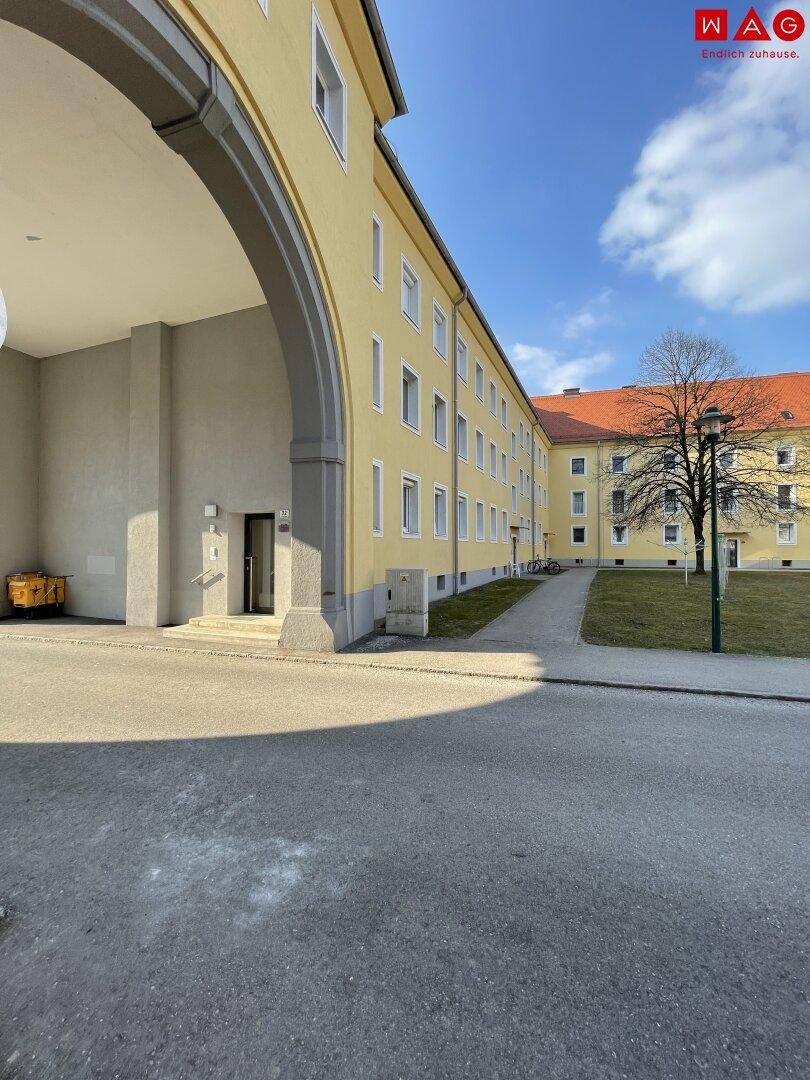 Eingangsbereich eines gelben Mehrfamilienhauses mit großem Torbogen und Zugang zu weiteren Gebäuden.