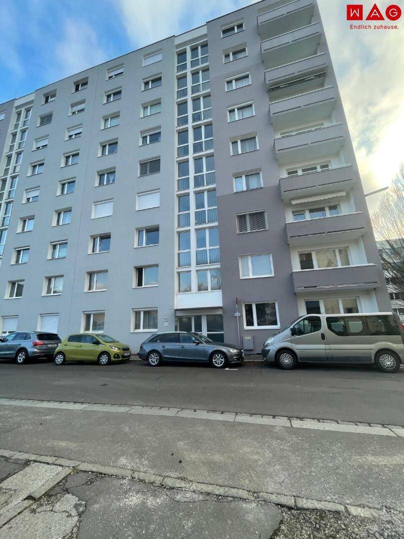 Ansicht der Gebäudefassade eines modernen Wohnhauses mit Balkonen und parkenden Autos auf der Straße.
