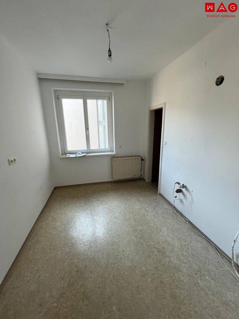 Leerer Raum mit Linoleumboden und Fenster, vorbereitet für eine Kücheninstallation.