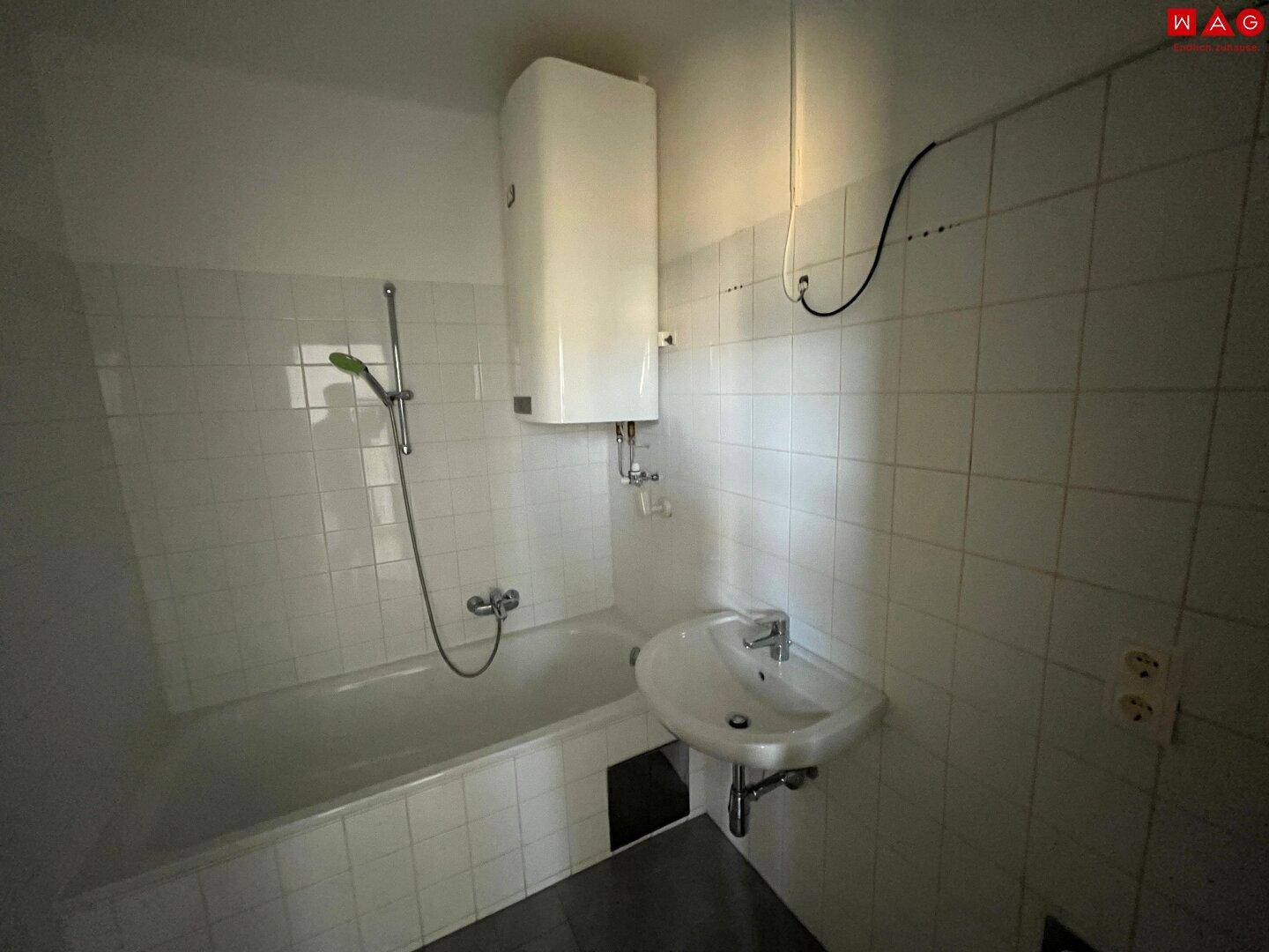 Badezimmer mit Badewanne, Waschbecken und weißen Fliesen, in originalem Zustand.