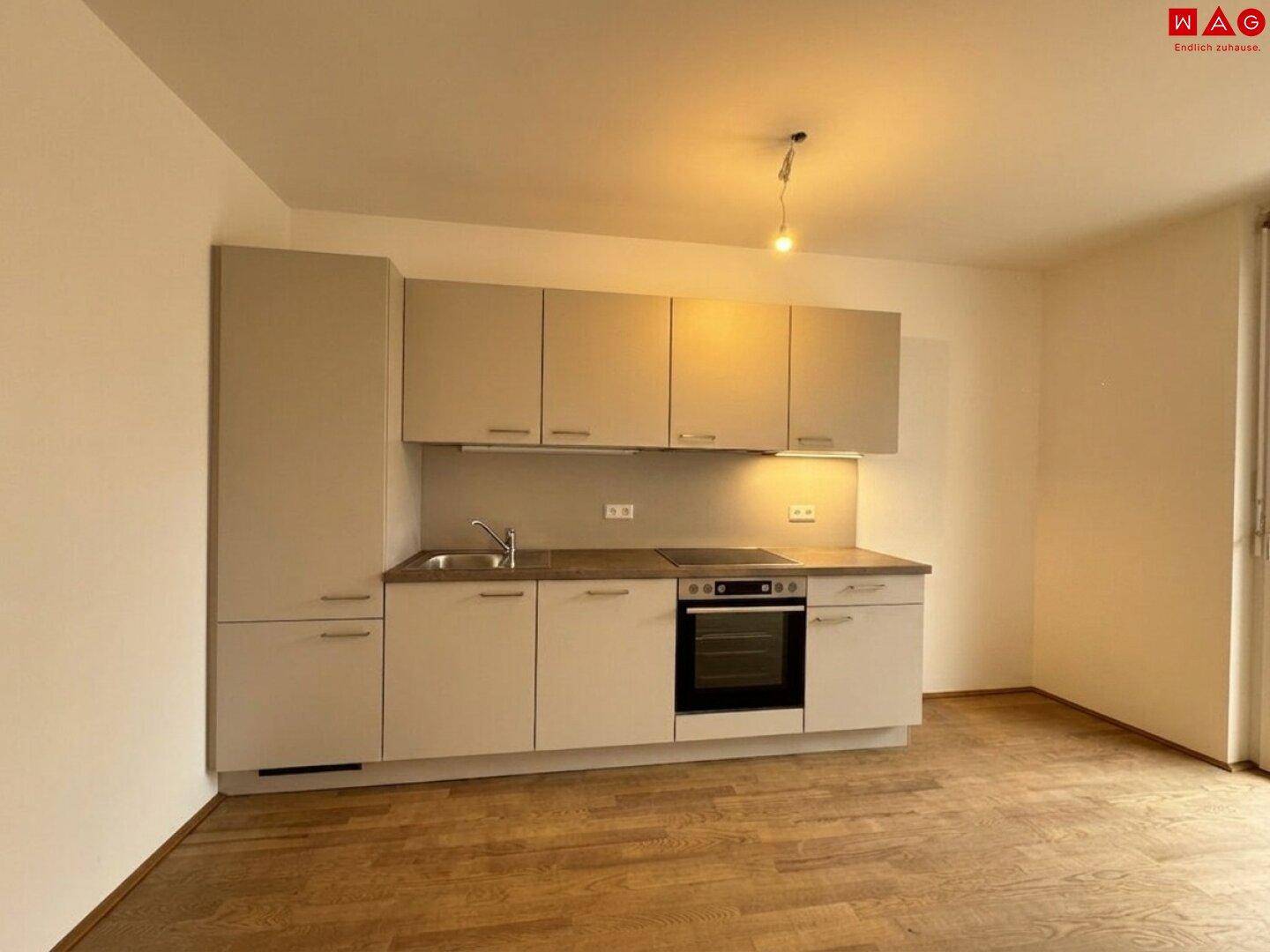 Kompakte Einbauküche mit hellen Schränken, integriertem Backofen und Kochfeld.