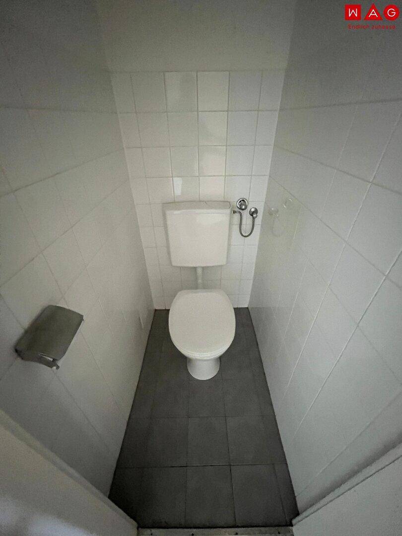 Separate Toilette mit weißen Fliesen und dunklem Fliesenboden.