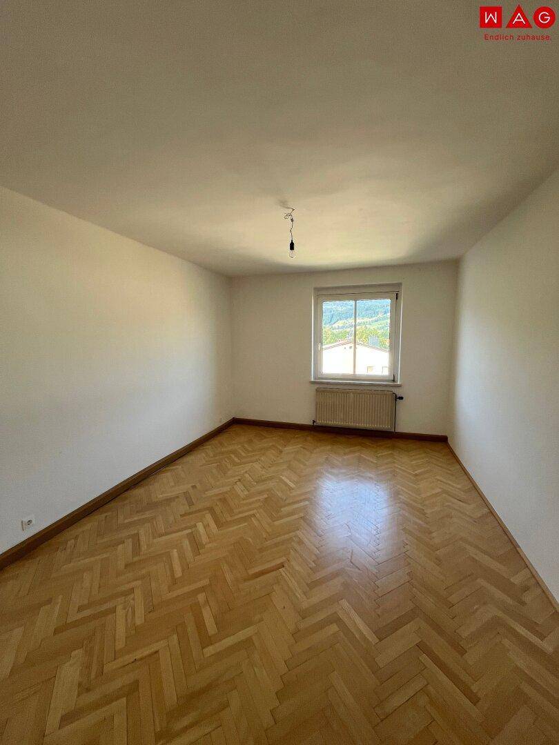 Leeres Zimmer mit Fischgrätparkettboden und Fenster mit Bergblick.
