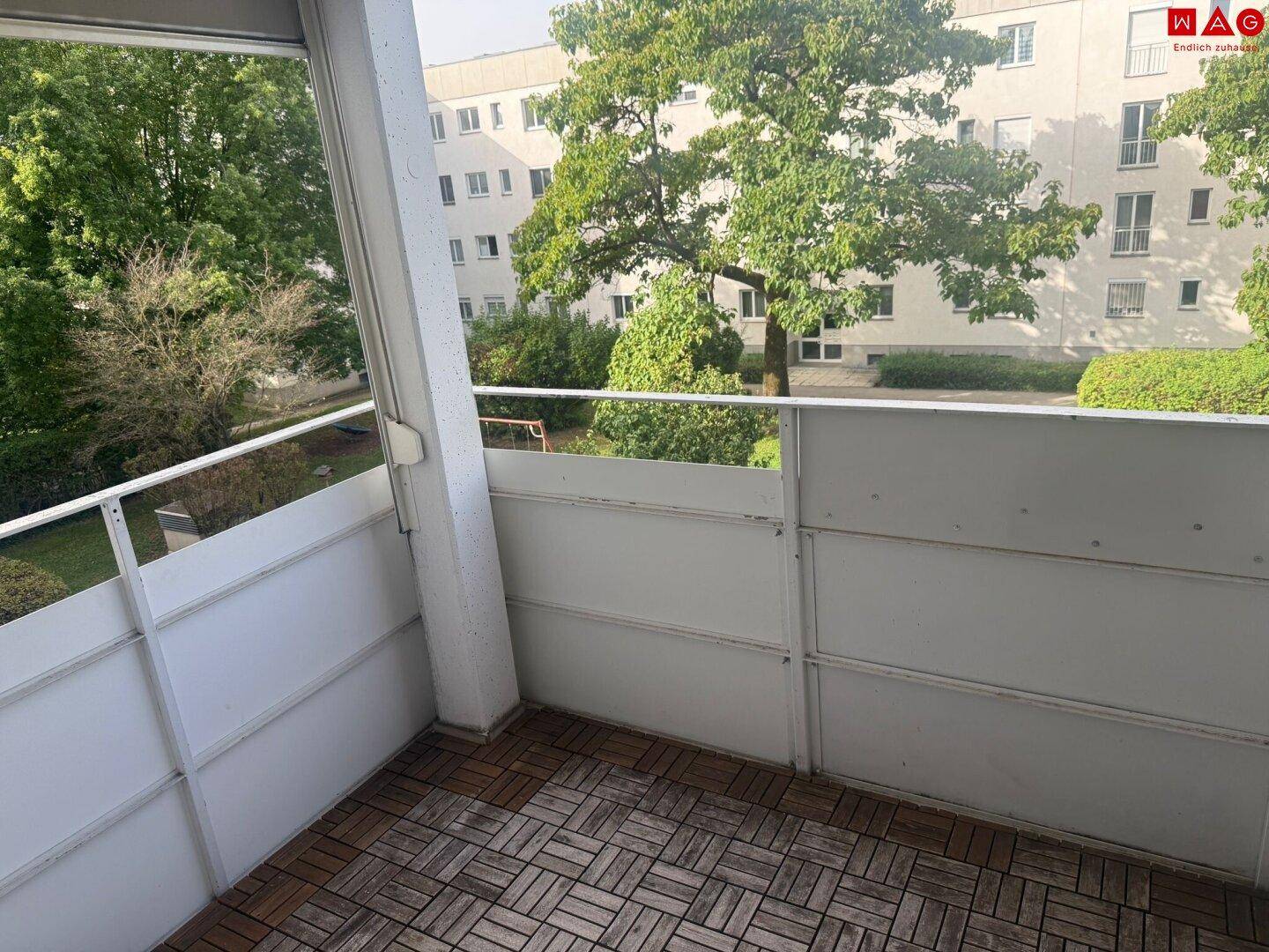 Balkon mit Holzbodenfliesen und einem angenehmen Blick ins Grüne der Wohnanlage.