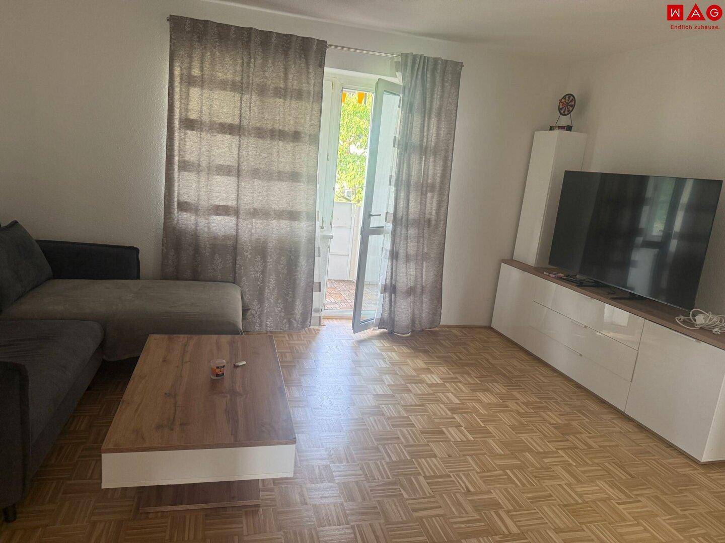Gemütliches Wohnzimmer mit Parkettboden, Sofa und direktem Zugang zum Balkon.