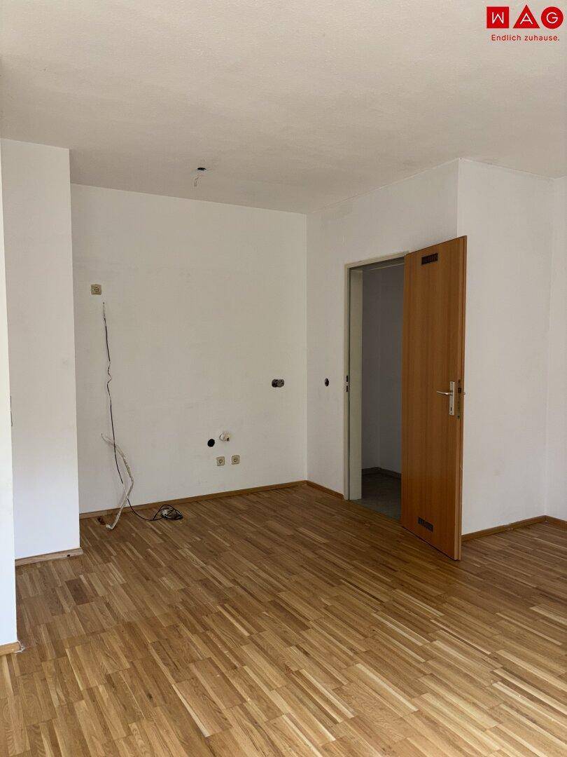 Leerer Raum mit Parkettboden, weißen Wänden und offener Tür zu einem angrenzenden Zimmer.