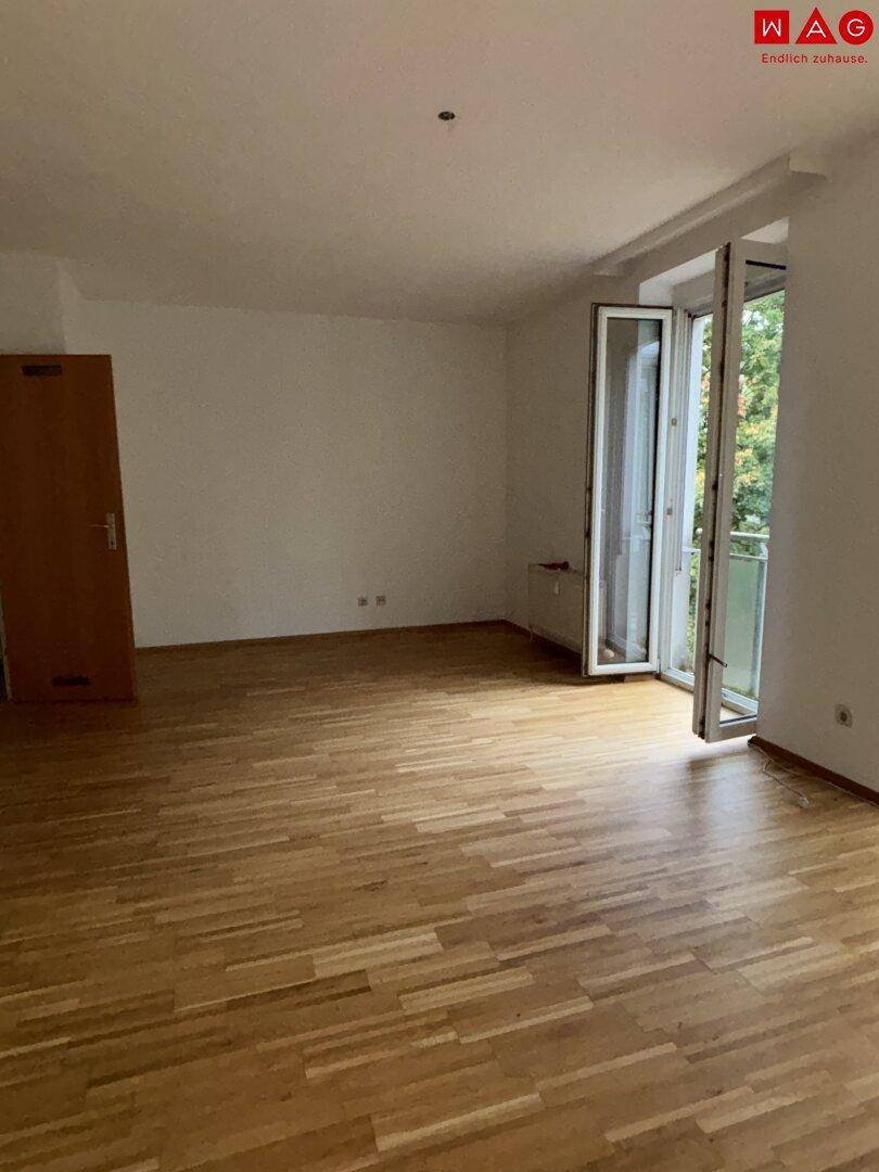 Geräumiger, heller Innenraum mit Holzboden und großen Fenstern, die viel Tageslicht hereinlassen.