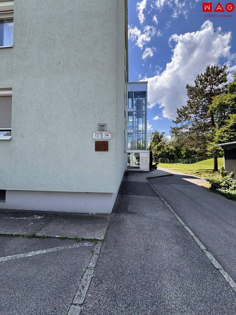 Eingangsbereich des Wohnhauses mit modernem Glasaufzug und Hausnummern.