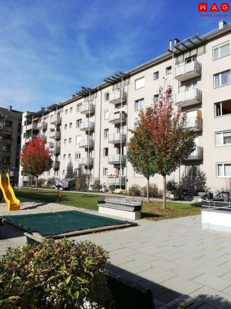 Gemeinschaftlicher Außenbereich mit Spielplatz, Rutsche und Bäumen vor dem Wohngebäude, ideal für Familien.
