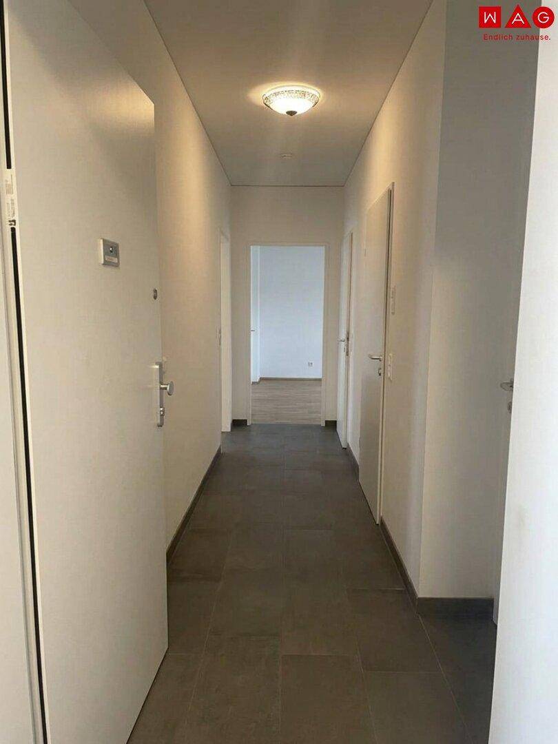 Heller Flur mit Fliesenboden und weißen Wänden, der zu den verschiedenen Räumen der Wohnung führt.