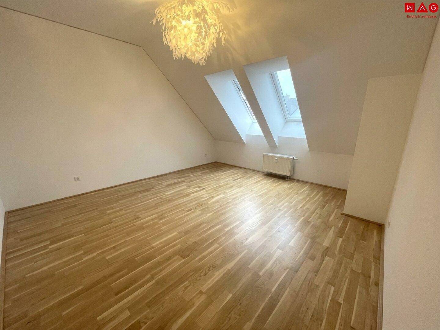 Helles Schlafzimmer mit Holzboden, Heizkörper und zwei Dachfenstern unter der schrägen Decke.