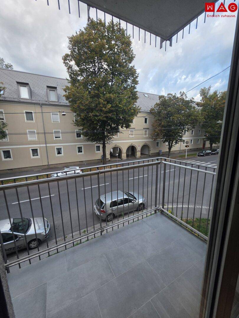 Balkon mit Blick auf die Straße und gegenüberliegende Gebäude, ausgestattet mit Fliesenboden und Geländer.