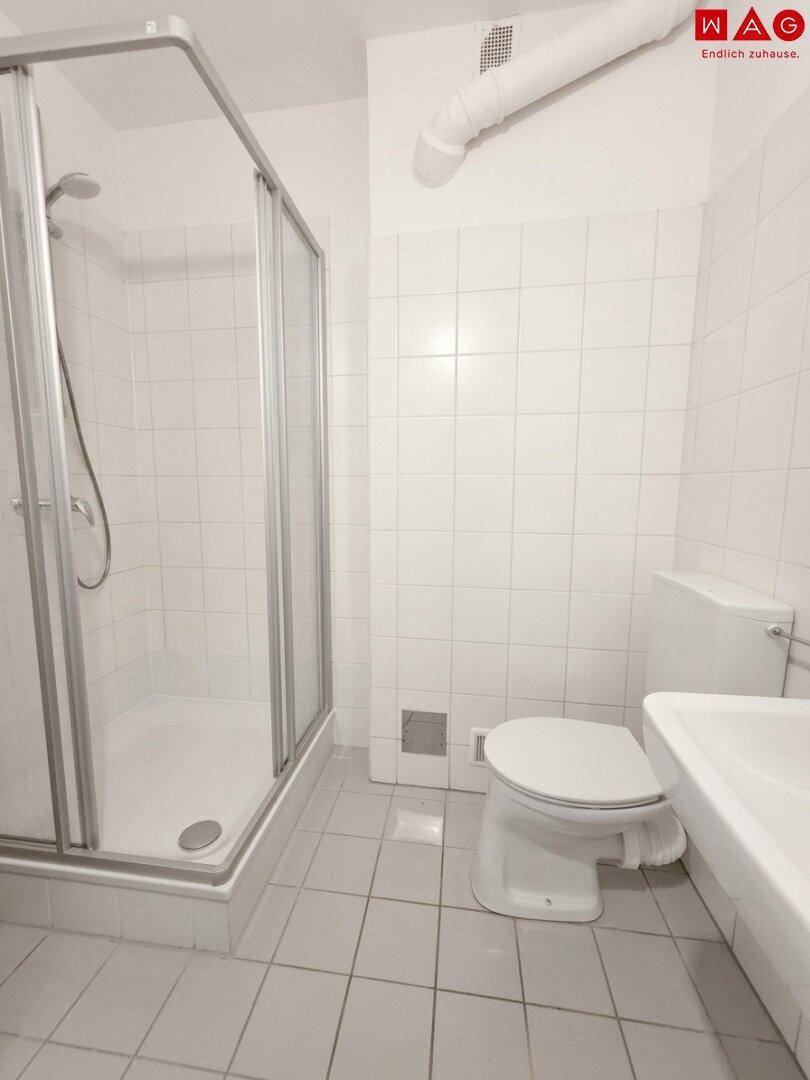 Funktionales Badezimmer mit Duschkabine, WC und Waschbecken, komplett mit weißen Fliesen ausgestattet.