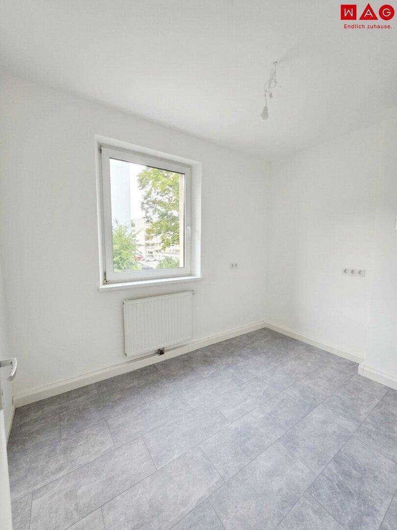 Unmöbliertes Zimmer mit großem Fenster, Fliesenboden und Heizkörper, ideal als Schlaf- oder Arbeitszimmer.