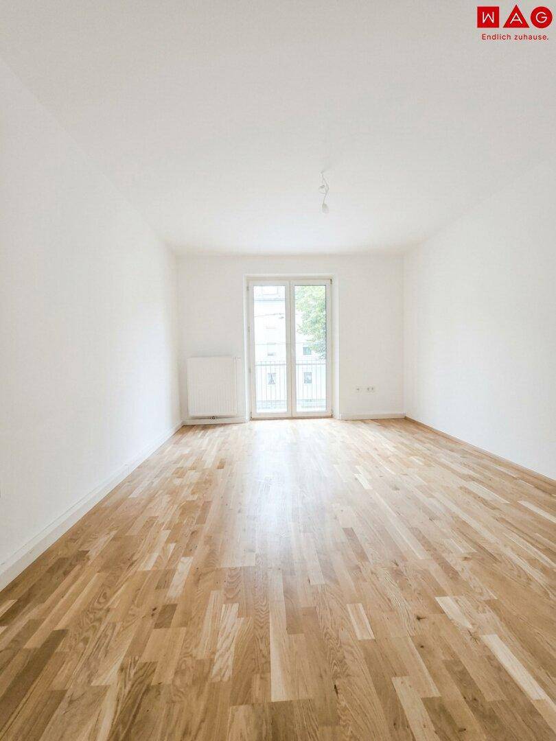 Helles, unmöbliertes Zimmer mit Eichenparkett und Zugang zu einem französischen Balkon.