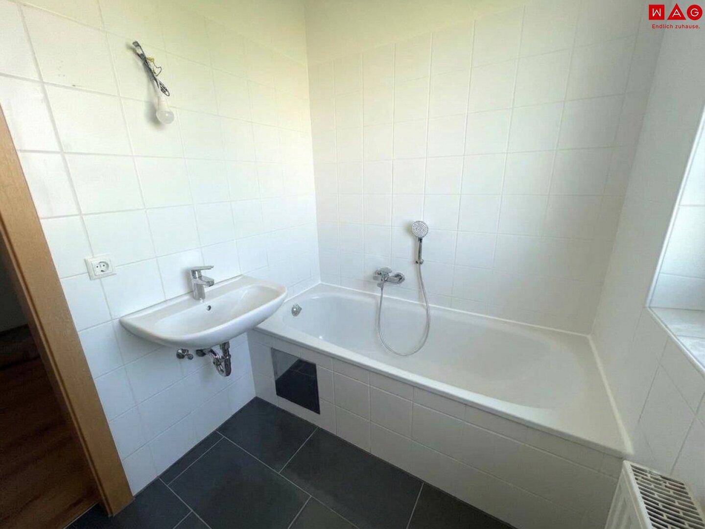 Helles Badezimmer mit Badewanne, Waschbecken und weißen Wandfliesen, funktional und sauber.