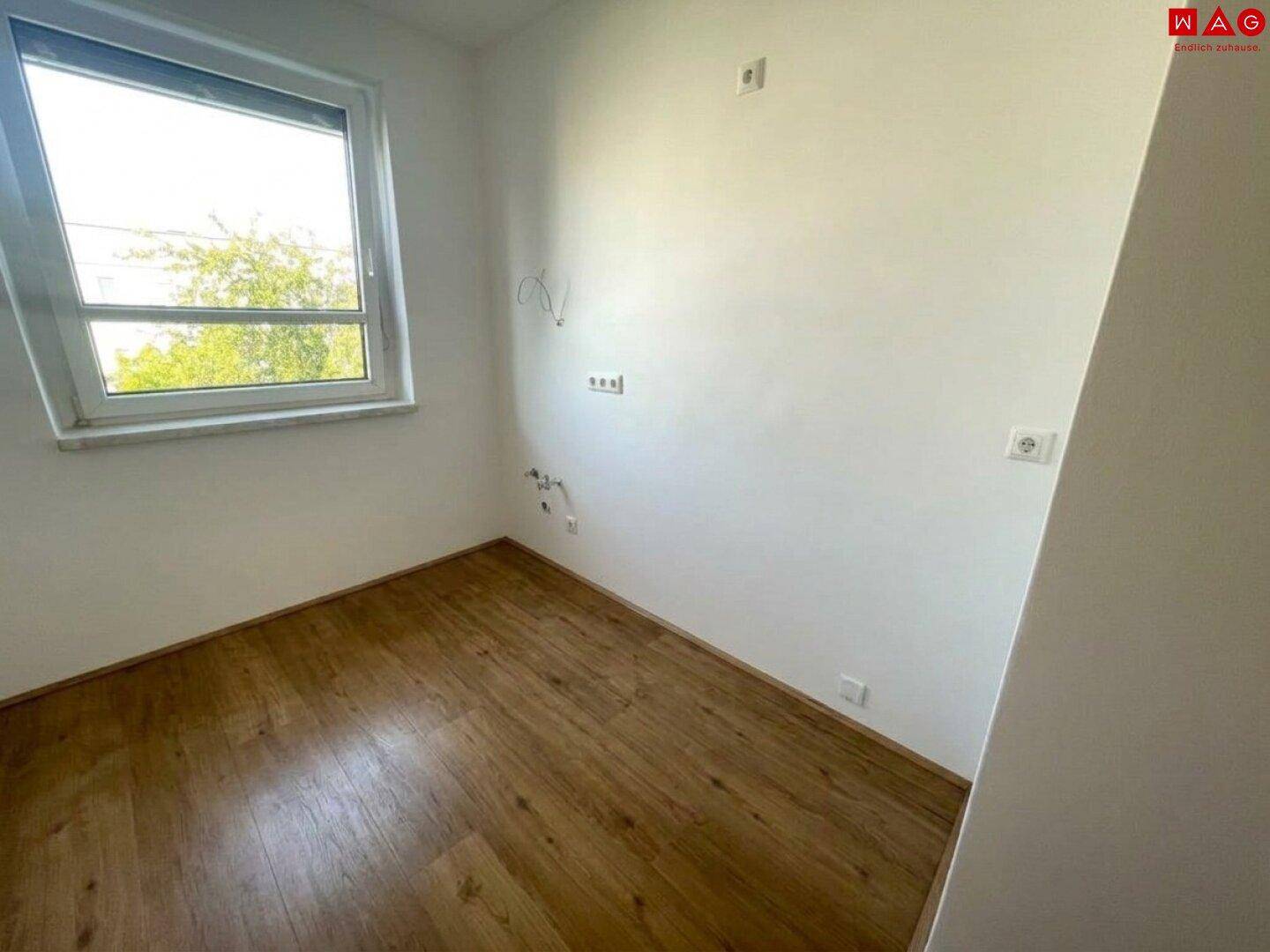 Leerer Raum mit Fenster und Laminatboden, vorbereitet für eine individuelle Nutzung.
