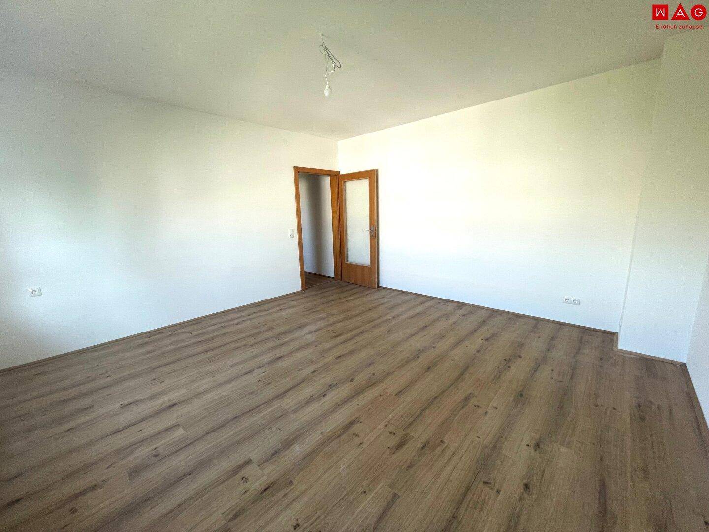 Leerer, heller Raum mit Laminatboden und Doppeltür, der vielseitig nutzbar ist.