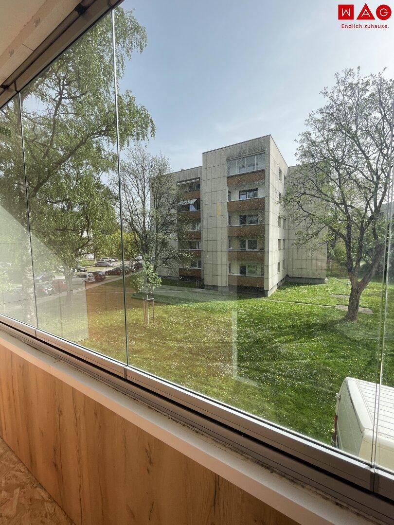 Verglaster Balkon mit Blick auf die grüne Umgebung und das Wohngebäude.
