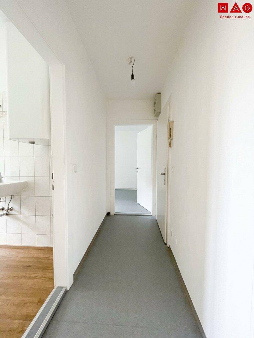 Heller Flur mit grauem Boden, weißen Wänden und Zugang zu weiteren Räumen der Wohnung.