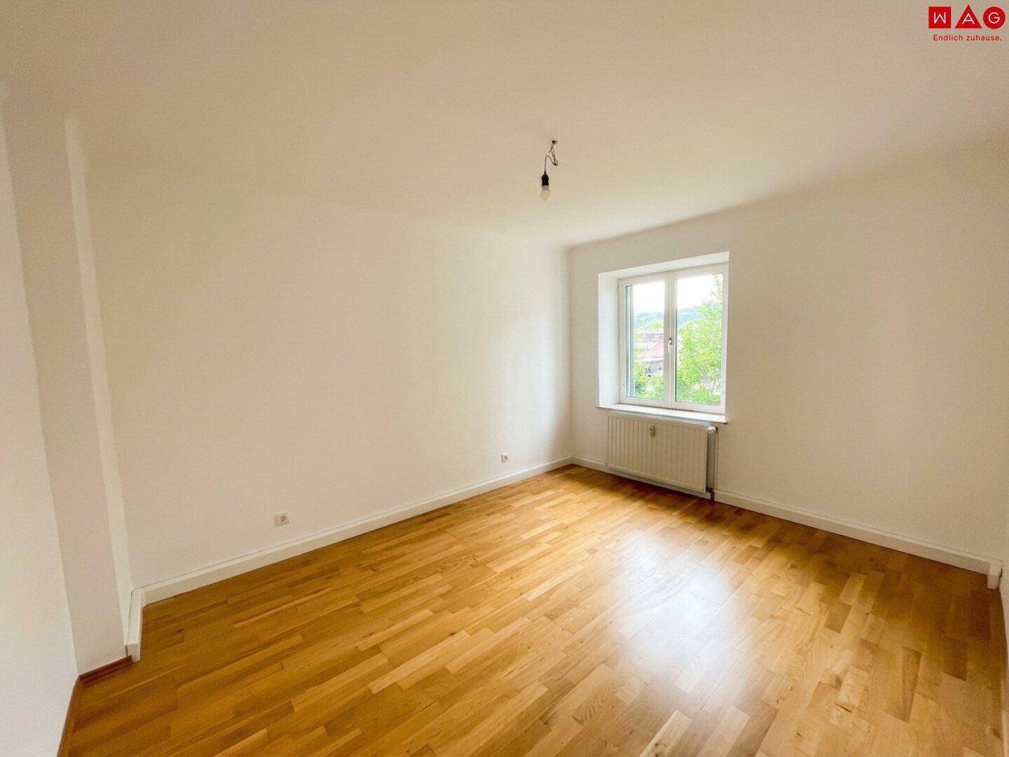 Helles Schlafzimmer mit schönem Parkettboden und Blick ins Grüne durch das Fenster.
