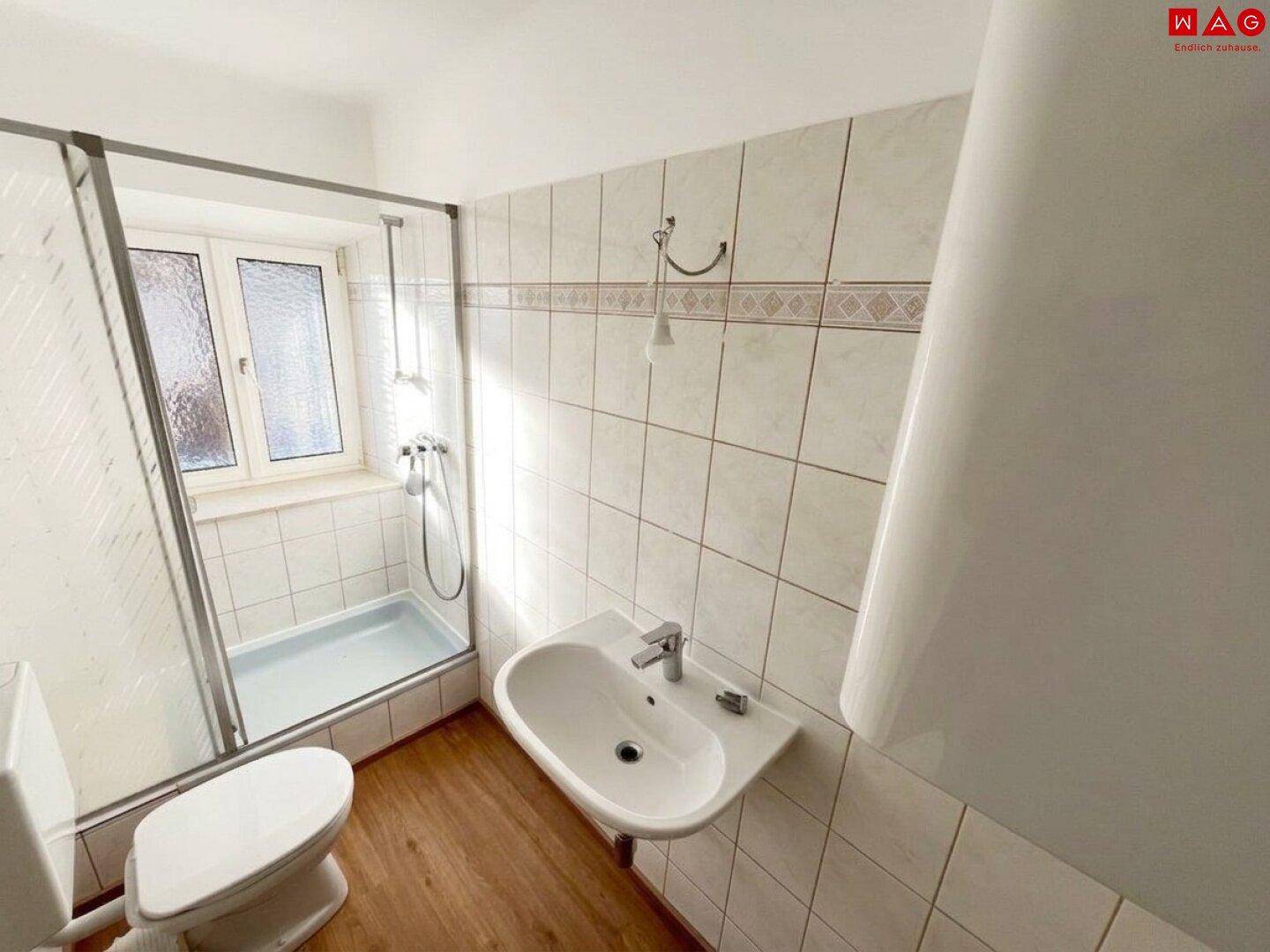 Funktionales Badezimmer mit Dusche, WC, Waschbecken und Fenster für natürliches Tageslicht.