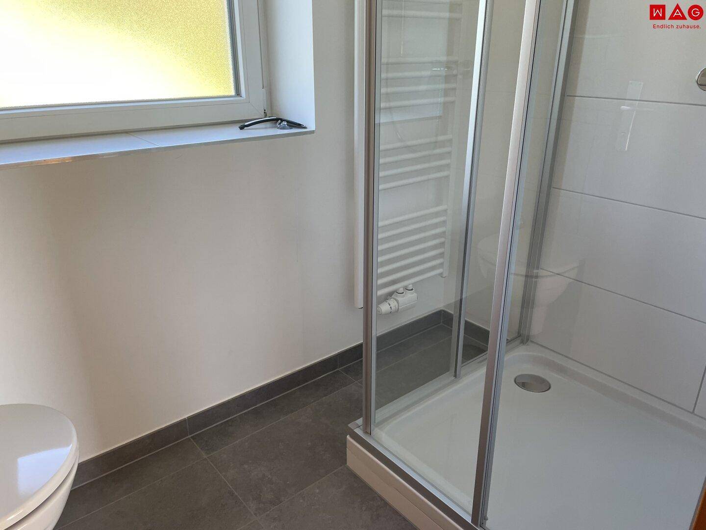Modernes Badezimmer mit Duschkabine, beheiztem Handtuchhalter und Fenster für Tageslicht.