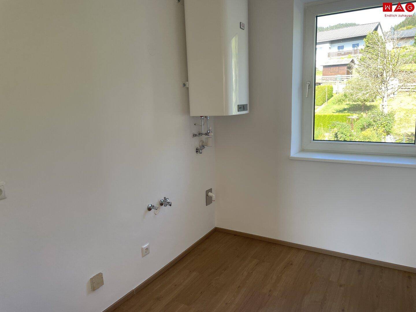 Hauswirtschaftsraum mit Warmwasserboiler und Anschlüssen für Waschmaschine, mit Blick ins Grüne.