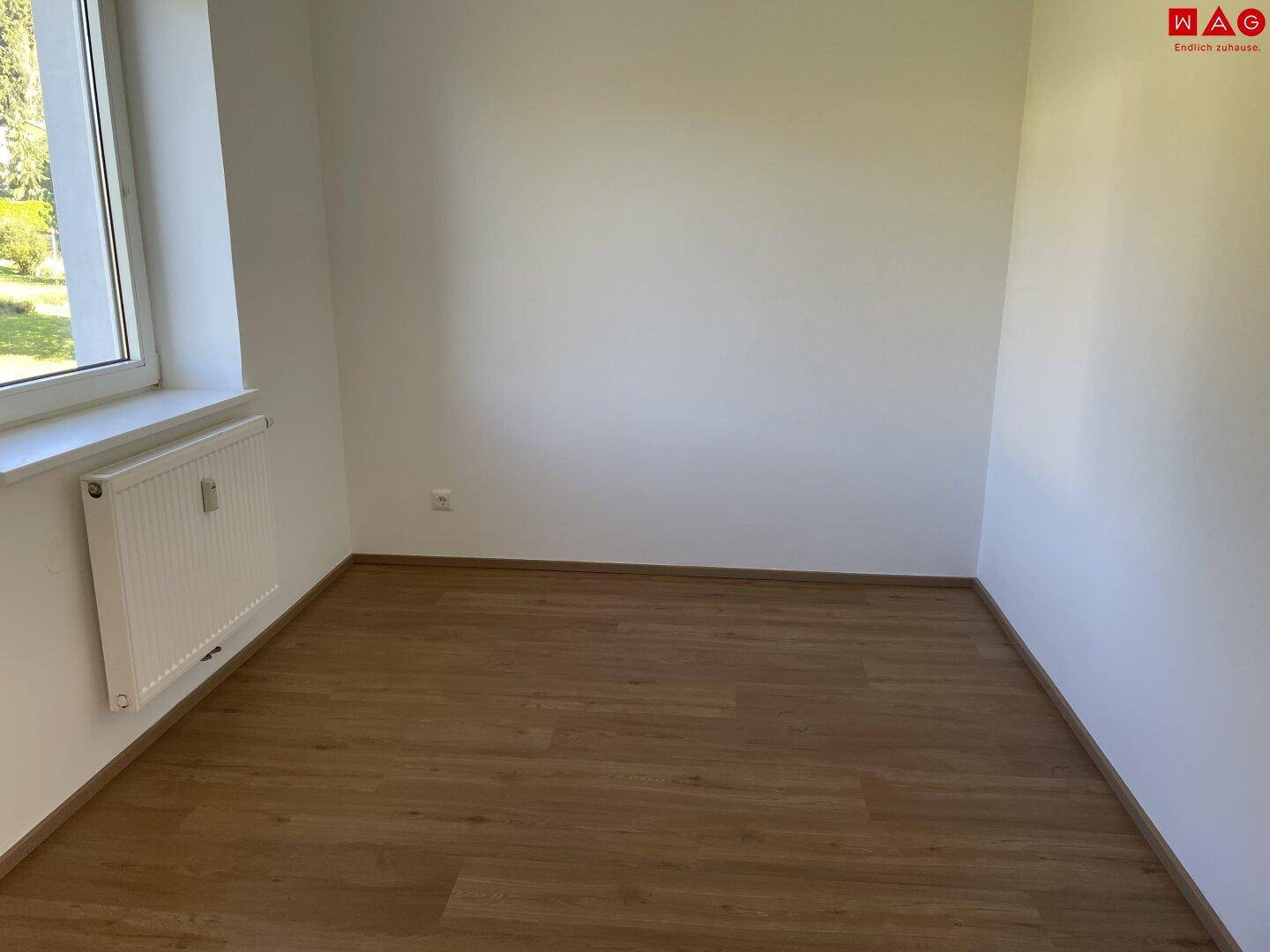 Geräumiges, leeres Zimmer mit Laminatboden und großem Fenster, ideal als Schlafzimmer.