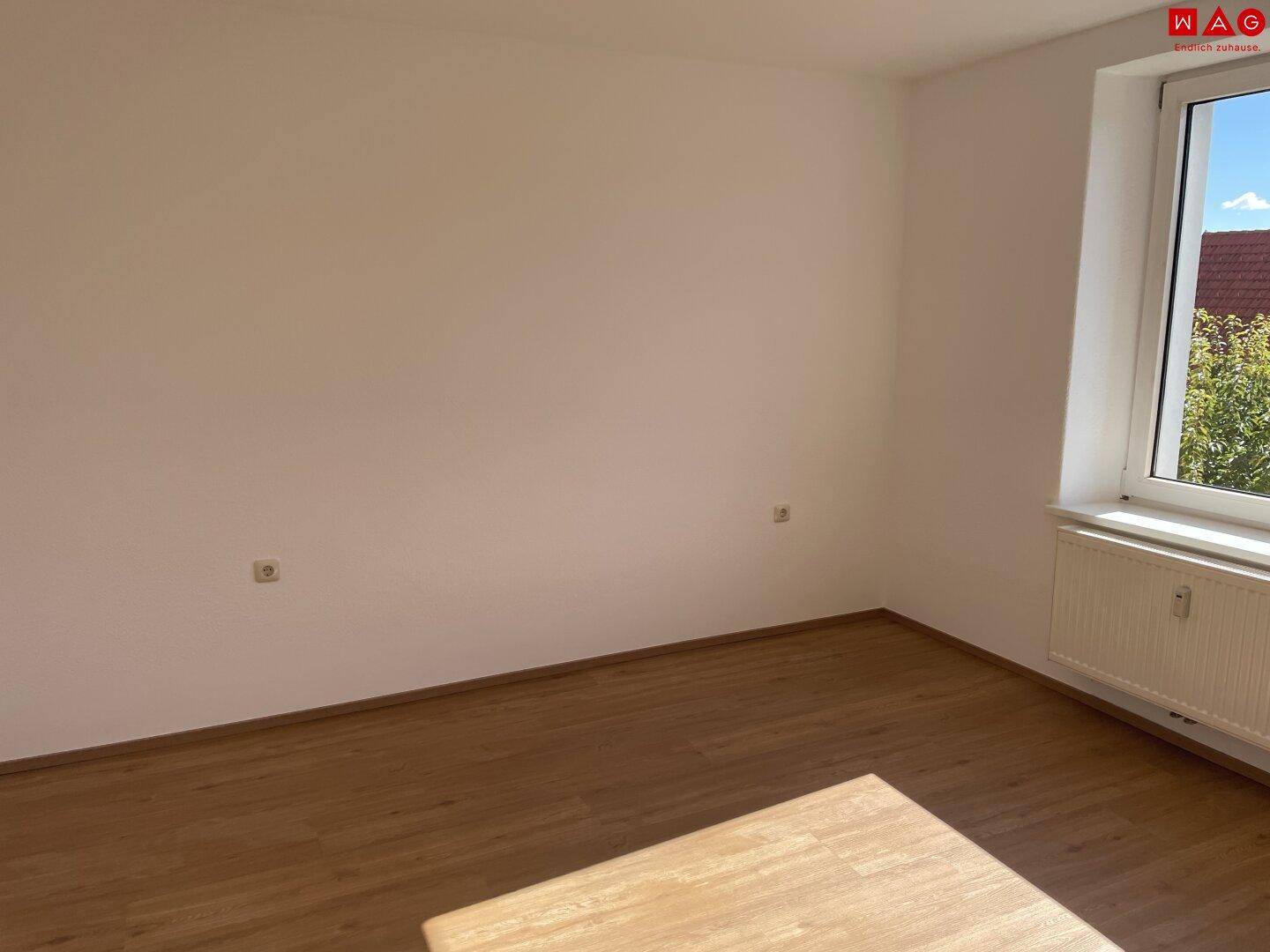 Geräumiges, leeres Zimmer mit Holzboden und Fenster, das viel Tageslicht hereinlässt.