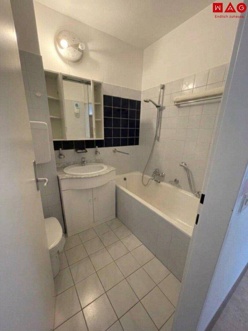 Funktionales Badezimmer mit Badewanne, Duschvorrichtung und Fliesen an Wänden und Boden.