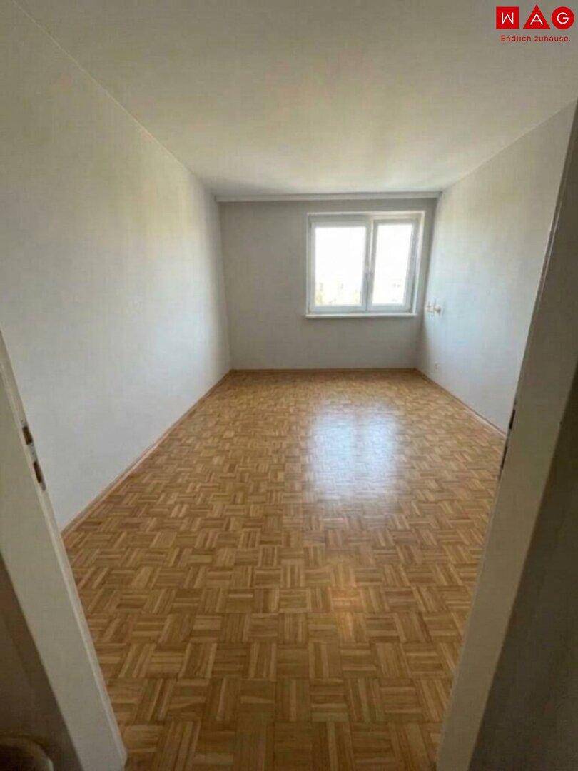 Leeres Schlafzimmer mit Parkettboden und einem großen Fenster, bereit zur individuellen Gestaltung.