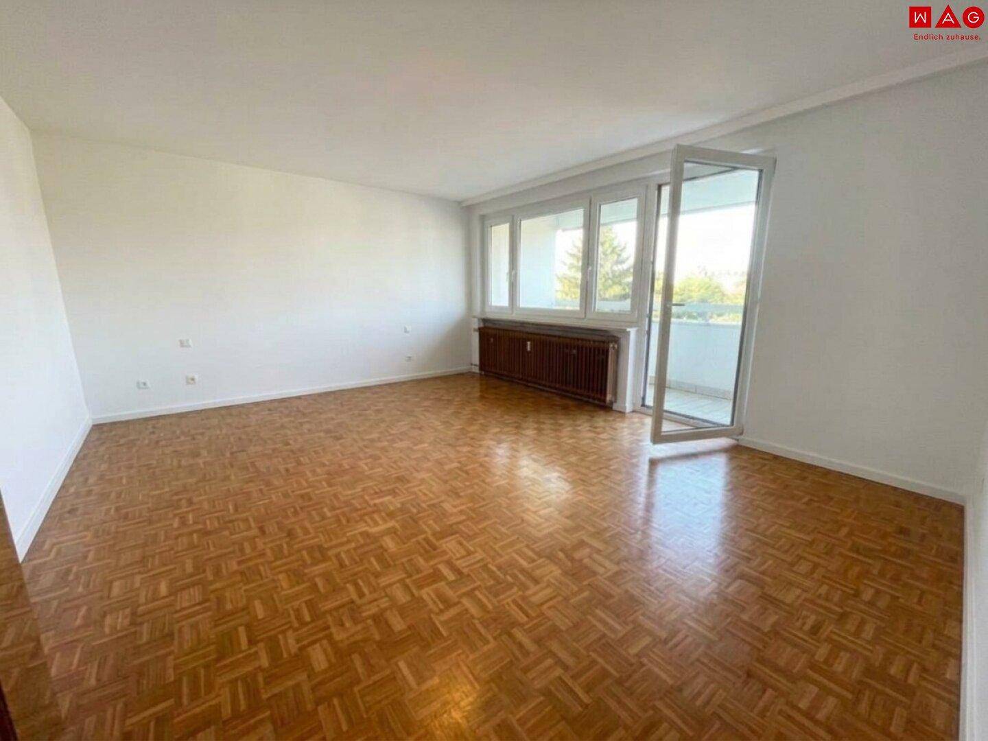 Geräumiges Wohnzimmer mit Parkettboden und großem Fenster mit Balkonzugang.